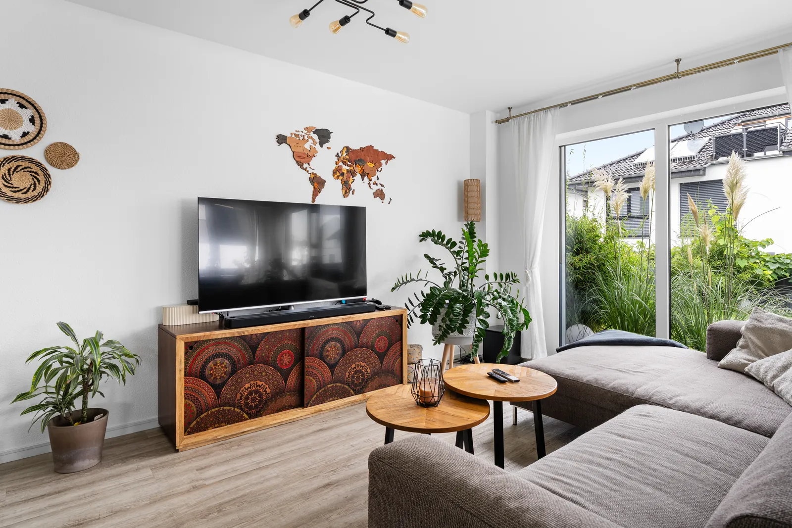 Wohnzimmer als fertiges Foto: der Raum ist hell, durch die Fensterfront sieht man Garten und Himmel.